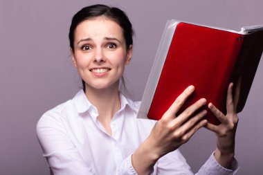 beyaz gömlekli kız elinde kırmızı bir defter tutar