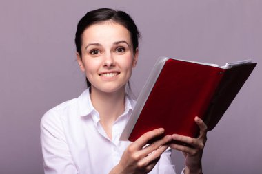 beyaz gömlekli kız elinde kırmızı bir defter tutar