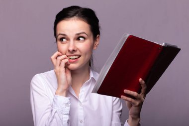 beyaz gömlekli kız elinde kırmızı bir defter tutar