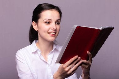 beyaz gömlekli kız elinde kırmızı bir defter tutar
