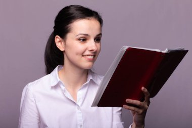 beyaz gömlekli kız elinde kırmızı bir defter tutar