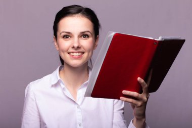 Beyaz gömlekli güzel bir kız elinde bir defter tutuyor.