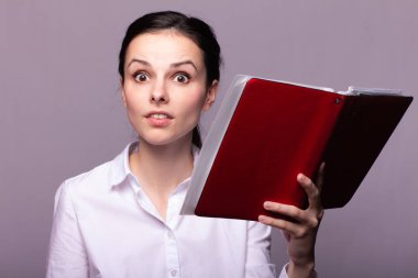 beyaz gömlekli kız elinde kırmızı bir defter tutar