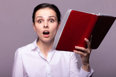 beyaz gömlekli kız elinde kırmızı bir defter tutar