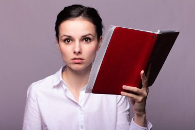 beyaz gömlekli kız elinde kırmızı bir defter tutar