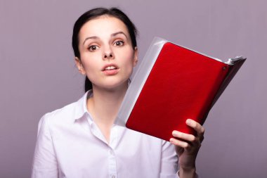 beyaz gömlekli kız elinde kırmızı bir defter tutar