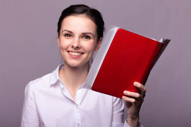 Beyaz gömlekli güzel bir kız elinde bir defter tutuyor.