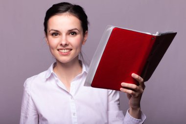 beyaz gömlekli kız elinde kırmızı bir defter tutar