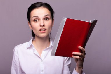 beyaz gömlekli kız elinde kırmızı bir defter tutar