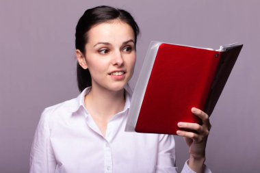 beyaz gömlekli kız elinde kırmızı bir defter tutar