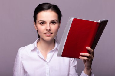 beyaz gömlekli kız elinde kırmızı bir defter tutar