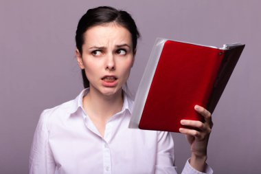 beyaz gömlekli kız elinde kırmızı bir defter tutar