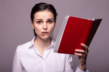 Beyaz gömlekli güzel bir kız elinde bir defter tutuyor.