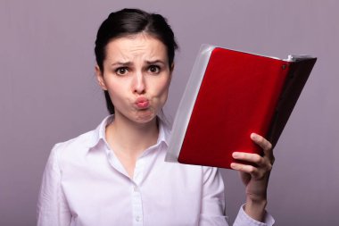 Beyaz gömlekli güzel bir kız elinde bir defter tutuyor.