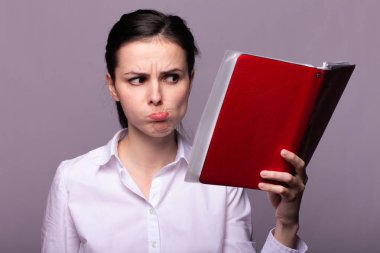 beyaz gömlekli kız elinde kırmızı bir defter tutar