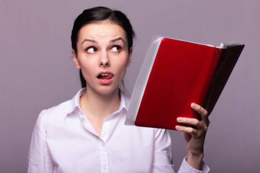 beyaz gömlekli kız elinde kırmızı bir defter tutar