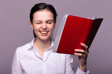 beyaz gömlekli kız elinde kırmızı bir defter tutar