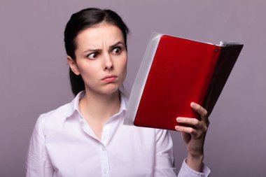 beyaz gömlekli kız elinde kırmızı bir defter tutar