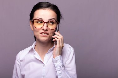 Beyaz gömlekli ve gözlüklü güzel kız telefonla konuşuyor.