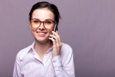 Beyaz gömlekli ve gözlüklü güzel kız telefonla konuşuyor.