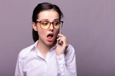 Beyaz gömlekli ve gözlüklü güzel kız telefonla konuşuyor.