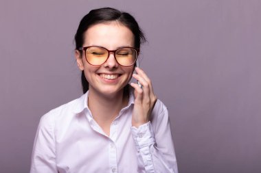 Beyaz gömlekli ve gözlüklü güzel kız telefonla konuşuyor.