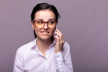 Beyaz gömlekli ve gözlüklü güzel kız telefonla konuşuyor.
