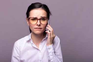 Beyaz gömlekli ve gözlüklü güzel kız telefonla konuşuyor.
