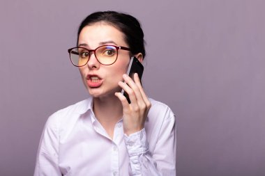 Beyaz gömlekli ve gözlüklü güzel kız telefonla konuşuyor.