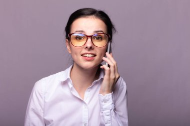 Beyaz gömlekli ve gözlüklü güzel kız telefonla konuşuyor.