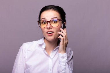 Beyaz gömlekli ve gözlüklü güzel kız telefonla konuşuyor.