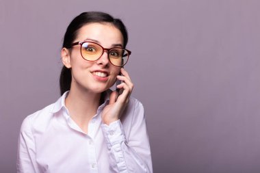 Beyaz gömlekli ve gözlüklü güzel kız telefonla konuşuyor.