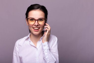 Beyaz gömlekli ve gözlüklü güzel kız telefonla konuşuyor.