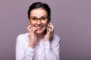 Beyaz gömlekli ve gözlüklü güzel kız telefonla konuşuyor.