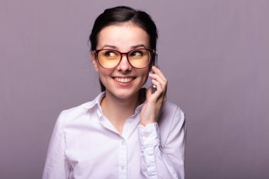 Beyaz gömlekli ve gözlüklü güzel kız telefonla konuşuyor.