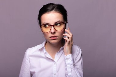 Beyaz gömlekli ve gözlüklü güzel kız telefonla konuşuyor.