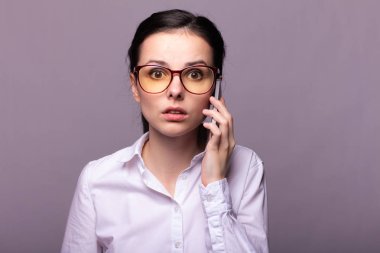Beyaz gömlekli ve gözlüklü güzel kız telefonla konuşuyor.