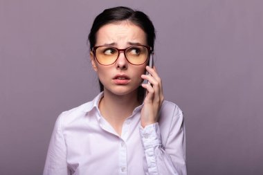Beyaz gömlekli ve gözlüklü güzel kız telefonla konuşuyor.
