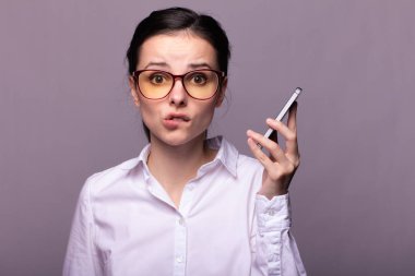 Beyaz gömlekli ve gözlüklü güzel kız telefonla konuşuyor.