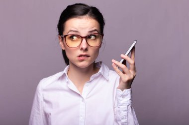Beyaz gömlekli ve gözlüklü güzel kız telefonla konuşuyor.