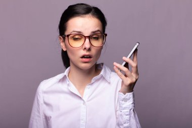 Beyaz gömlekli ve gözlüklü güzel kız telefonla konuşuyor.