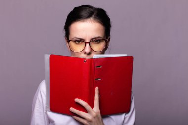 beyaz gömlek ve gözlük kız elinde kırmızı bir defter tutar