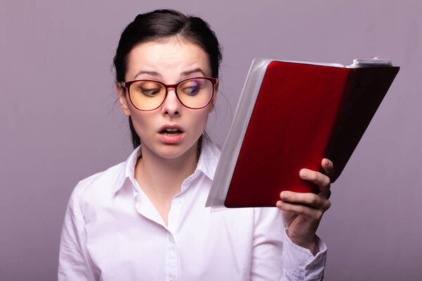 girl in a white shirt and glasses holds a red notebook in her hand