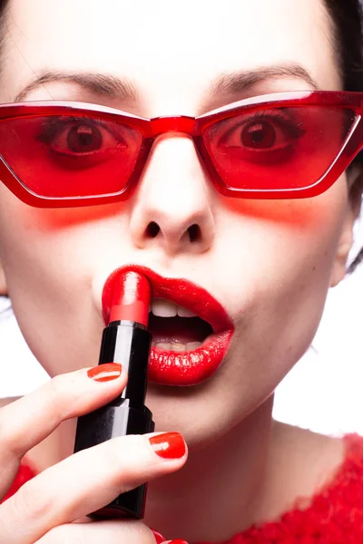 girl in a red sweater and red glasses paints her lips with red lipstick