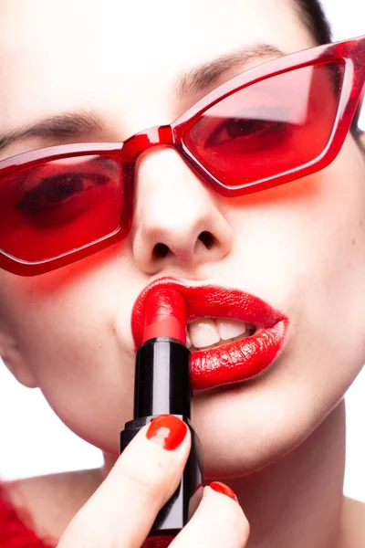 girl in a red sweater and red glasses paints her lips with red lipstick