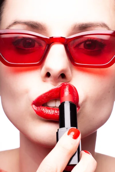 girl in a red sweater and red glasses paints her lips with red lipstick