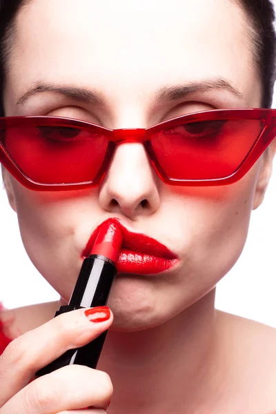 girl in a red sweater and red glasses paints her lips with red lipstick