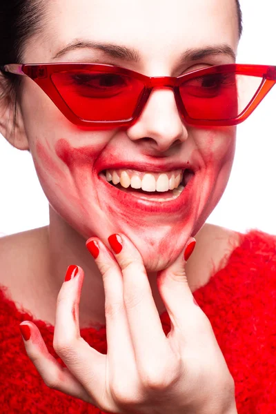 a girl in a red sweater and red glasses smears lipstick on her face