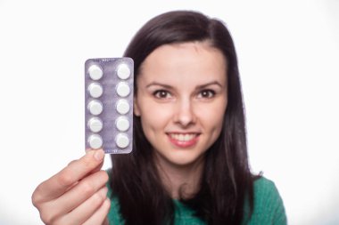 Yeşil kazaklı güzel bir kız elinde bir paket hap tutuyor.