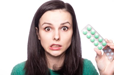 Yeşil kazaklı güzel bir kız elinde bir paket hap tutuyor.